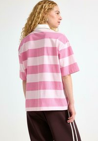 Polo shirt oversize a maniche corte con righe orizzontali rosa e rosa chiaro, realizzata in un tessuto morbido, con colletto bianco.