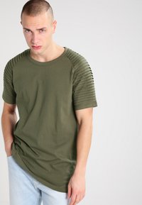 Camiseta verde olivo hecha de algodón, con textura acanalada en los hombros, mangas cortas y diseño de cuello redondo.