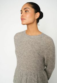 Lichtgrijze peplumtrui gemaakt van een zachte, gestructureerde stof met een ronde halslijn en lange mouwen, gedetailleerd met subtiele gemêleerde patronen.