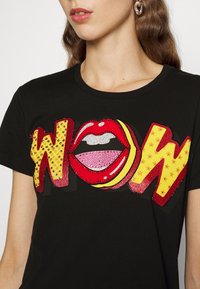 Černé tričko s výrazným nápisem "WOW", zdobené detaily červených rtů a barevnými kamínky. Krátké rukávy, design s kulatým výstřihem.