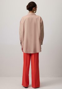 Garais piedurknes, gaiši rozā blūze ar apkakli, kopā ar platām, spilgti oranžām biksēm. Gluda tekstūra, pogām aizdarāmas piedurknes, brīvs piegriezums.