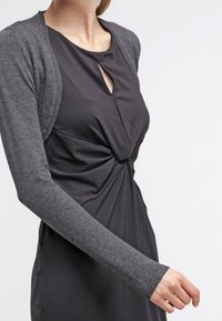 Grauer Strickcardigan über einem schwarzen Kleid mit verdrehtem Vorderteil und Schlüssellochausschnitt, ausgestattet mit langen Ärmeln und einer taillierten Silhouette.