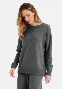 Pull en tricot gris à col large, avec des manches longues et un ourlet côtelé. Présente un design simple avec une texture lisse et un minimum de détails.
