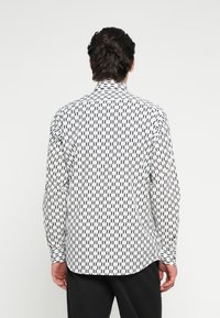Fekete-fehér mintás hosszú ujjú ing galléros nyakkal, geometriai mintázattal és sima anyagból. A hátoldalon gombos mandzsetta látható.