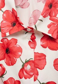 Blusa a maniche corte in tessuto morbido con grandi fiori di papavero rossi su sfondo bianco, con colletto a punta e chiusura con bottoni.