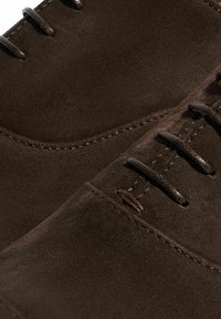 Scarpe in suede marrone con una texture liscia, design arrotondato e cinque occhielli per i lacci. Le cuciture decorative aumentano la durata.