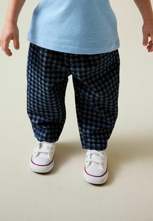 Navy and gray checkered pants with a baggy fit, paired with white sneakers featuring red accents, on a child. Blue top partially visible.