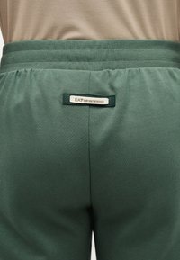 Πράσινο βαμβακερό παντελόνι φόρμας με ελαστική ζώνη μέσης. Διαθέτει ραμμένη ετικέτα επωνυμίας "EA7 EMPORIO ARMANI" στο πίσω μέρος. Ομαλή υφή, casual σχεδιασμός.