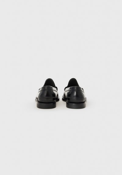 Chaussures en cuir noir avec une texture lisse, dos arrondi, petit talon et détails de couture subtils. Pas d'ornements visibles.