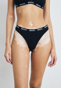 Zwarte katoenen stringonderbroek met een hoge uitsnijding en een merkband. Glad materiaal, minimalistische stijl, comfortabel passend.