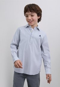 Camicia a maniche lunghe a righe in azzurro chiaro e bianco, con patta a bottoni e piccolo logo teschio ricamato in blu navy sul petto.