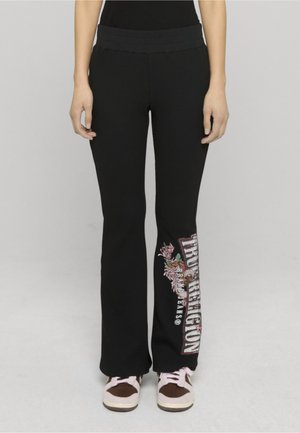 Czarne dzwonowe spodnie dresowe z fakturowanej dzianiny z kolorowym kwiatowym wzorem i napisem „True Religion” po lewej stronie.
