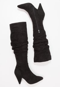 Botas negras hasta la rodilla hechas de suave ante, con un diseño holgado, punta afilada y cremallera lateral. Tacones altos y en forma de cono.