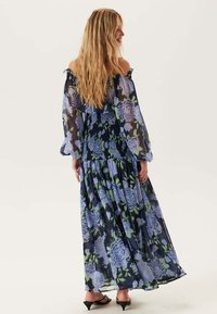 Maxi-jurk in doorzichtig materiaal, met een donker bloemenpatroon in tinten blauw en groen. Off-shoulder ontwerp en lange mouwen met ruches.