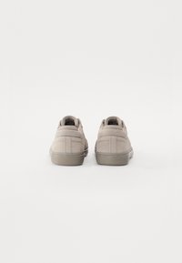 Sneakers din suede bej cu un design low-top, vârf rotund, guler căptușit și talpă din cauciuc texturată. Șireturi plate și cusături minimaliste.