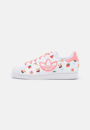 Zapatilla blanca con acentos rosas, adornada con estampados de frutas coloridas y helados. Punta redondeada, suela de goma y diseño clásico de tres rayas.