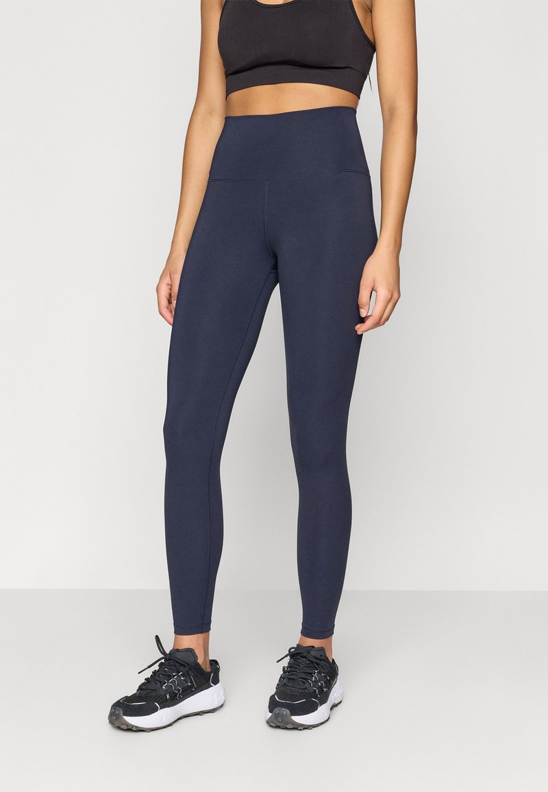 Ναυτικά κολάν ψηλής μέσης φτιαγμένα από ελαστικό ύφασμα, με απλή υφή και επίπεδες ραφές, συνδυασμένα με μαύρα αθλητικά παπούτσια.