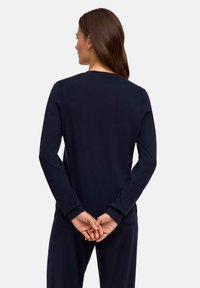 Marineblaues Langarmshirt aus geripptem Stoff, mit Rundhalsausschnitt und enganliegenden Bündchen. Das Modell hat die Hände hinter dem Rücken verschränkt.