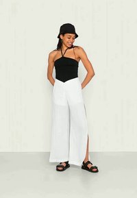 Top halter preto com alças finas, emparelhado com calças largas brancas de cintura alta com fendas laterais, complementado por um chapéu bucket preto e sandálias.
