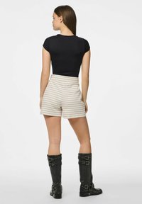 Crna prilagođena majica, prugaste kreme i bež kratke hlače, visoke crne čizme s kopčom. Outfit ima opušten kroj i kontrastne teksture.