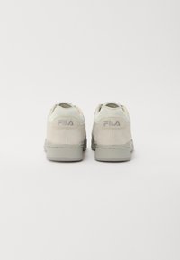 Beige Wildledersneaker mit glatter Textur und grauer Gummisohle. Die Rückseite ist mit "FILA" in hellem Grau geprägt. Einfaches und minimalistisches Design.