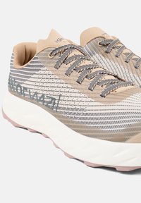 Beige and gray athletic shoes with a textured, patterned mesh upper, gray laces, and white sole featuring a pink accent.