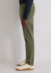 Zielone bawełniane spodnie o prostym kroju nogawek, wyposażone w boczne kieszenie i tylną kieszeń, zestawione z białymi trampkami i granatowym swetrem.