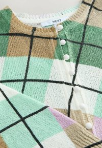 Cardigan en tricot présentant un motif à carreaux vert, menthe, blanc, marron et rose. Encolure ronde avec des boutons blancs sur le devant.
