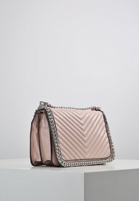Borsa a tracolla sintetica rosa trapuntata con catena argentata, caratterizzata da un motivo a zigzag e una forma rettangolare elegante.