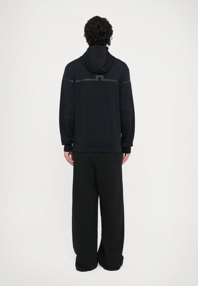 Μαύρο φούτερ με κουκούλα και άνετη εφαρμογή, με υφή στους ώμους και τσέπη καγκουρό. Συνδυάζεται με φαρδιά μαύρη παντελόνα.