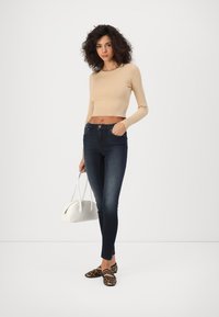 Un pull court beige à côtes, un jean skinny bleu foncé, des ballerines à imprimé animal, et un sac à main blanc. Textures lisses, design ajusté.
