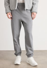 Pantalones de chándal grises hechos de una tela suave, con cinturilla y puños elásticos. Combinados con zapatillas deportivas blancas. Diseño simple y funcional.