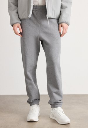 Pantalones de chándal grises hechos de una tela suave, con cinturilla y puños elásticos. Combinados con zapatillas deportivas blancas. Diseño simple y funcional.
