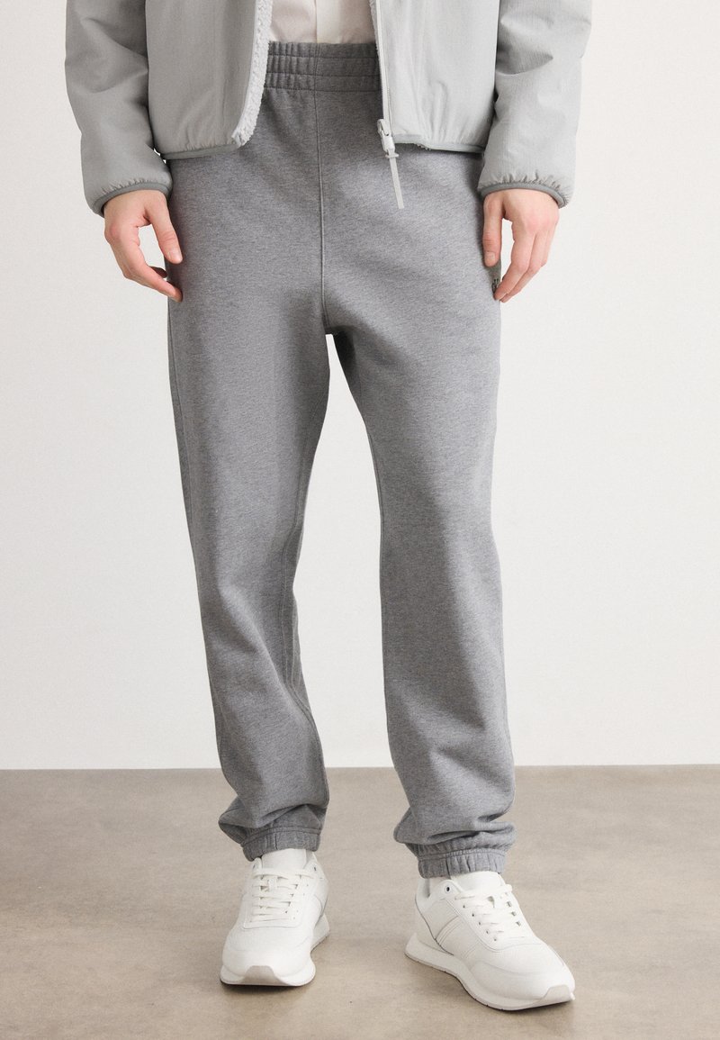 Pantalones de chándal grises hechos de una tela suave, con cinturilla y puños elásticos. Combinados con zapatillas deportivas blancas. Diseño simple y funcional.