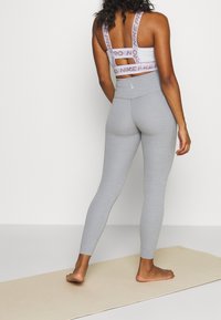 Leggings atletici grigi realizzati in tessuto elastico, con vita alta e texture liscia. Completati da un reggiseno sportivo con spalline decorate.
