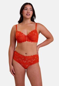 Conjunto de sujetador y braga de encaje rojo con bordes scallopados, patrones florales y tirantes ajustables; la textura transparente realza los detalles del diseño.