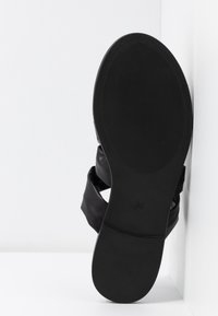 Sandale noire avec une tige en cuir lisse et une semelle en caoutchouc texturé. Le design comprend des sangles larges pour le soutien et le confort du pied.