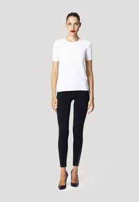 T-shirt bianco a maniche corte abbinato a leggings neri e tacchi alti neri, con un design semplice e lineare senza ulteriori motivi.