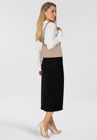 Borsa a tracolla beige trapuntata con un design strutturato, tracolla in catena e dettaglio logo a triangolo, abbinata a una camicia bianca e una gonna nera.