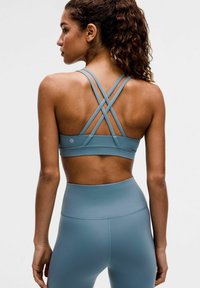 Brassière de sport turquoise avec bretelles croisées, présentant une texture lisse et un design minimaliste. Associée à un legging turquoise taille haute.