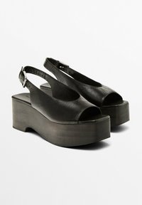 Svarta läderplattformssandaler med öppen tå, slingback-design och accent av silvermetallspänne. Sulan är tjock och texturerad.