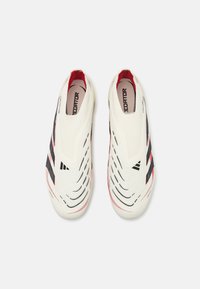 White slip-on sports shoes with black and red accents. Features wavy textured design and branding on the heel and insole. Smooth material.