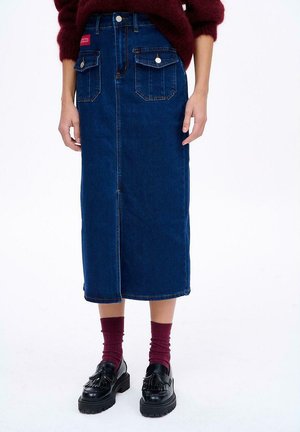 Ciemnoniebieska spódnica dżinsowa z przednim szwem, dwoma kieszeniami naszytymi i zapięciem na guziki. Połączona z czarnymi loafersami i bordowymi skarpetkami prążkowanymi.