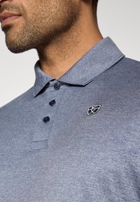 Μπλέ πόλο μπλούζα με γιακά, δύο κουμπιά και κεντητό λογότυπο στο στήθος. Μαλακό, υφασμάτινο υλικό.