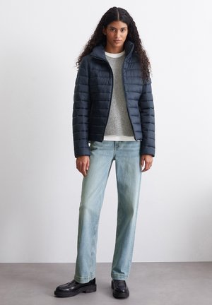 Marineblå dunjakke med horisontalt quiltet mønster, grå genser, lys denim jeans og svarte platå sko.
