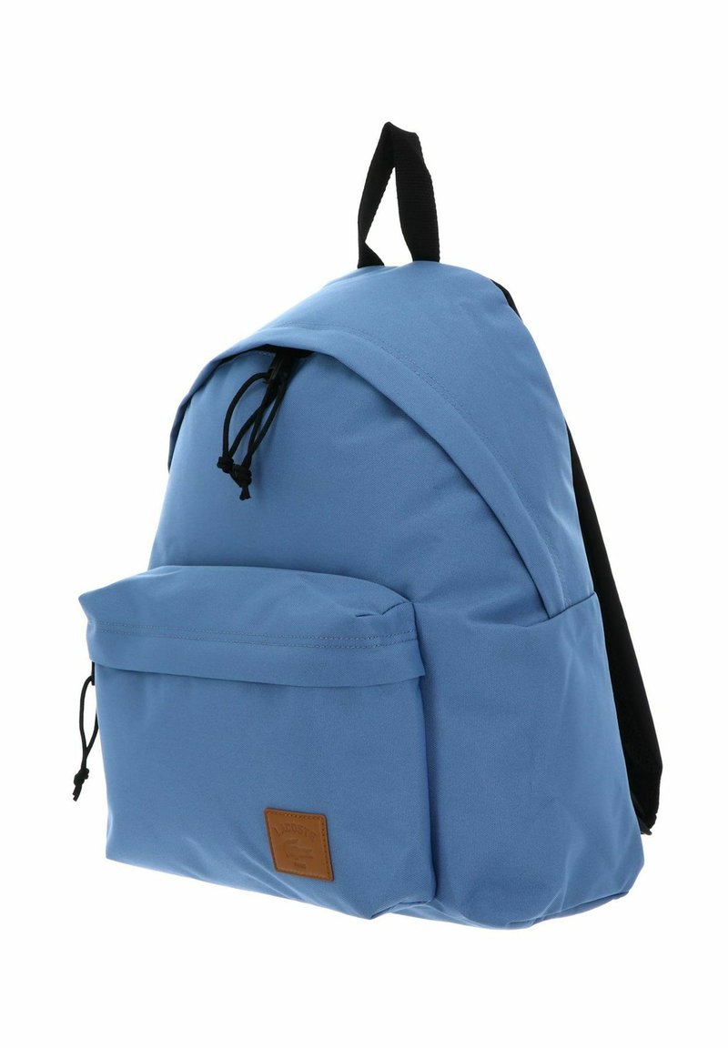 Hellblauer Stoffrucksack mit schwarzen Trägern, vordere Reißverschlusstasche und einem kleinen braunen Leder-Logo auf der Tasche.