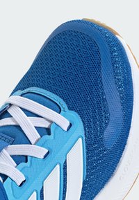 Blauer Sportschuh mit Mesh-Obermaterial, weißen Schnürsenkeln, Gummisohle und markanten blauen Akzenten. Verfügt über ein texturiertes Design und eine unterstützende Struktur.