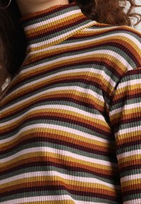 Pull à col roulé à manches longues en tissu côtelé, présentant des rayures horizontales de couleurs marron, or, vert et blanc, avec une coupe ajustée.