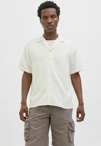 Korte ærmede cremefarvede skjorte med krave, der har et subtilt teksture mønster og knaplukning foran, parret med grå cargo-shorts.