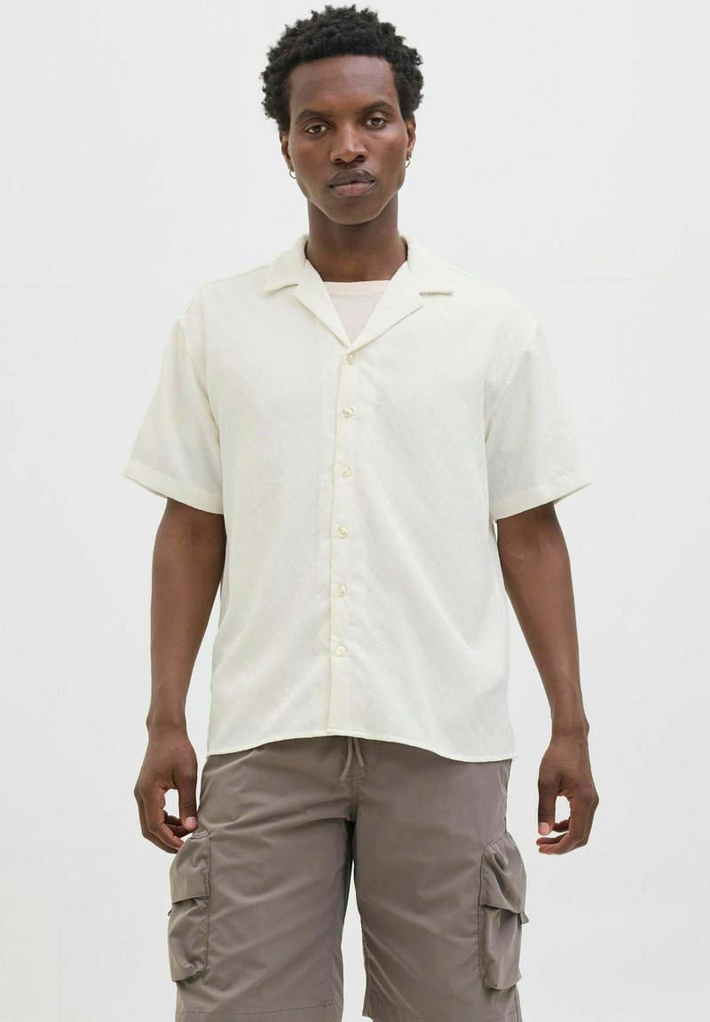 Korte ærmede cremefarvede skjorte med krave, der har et subtilt teksture mønster og knaplukning foran, parret med grå cargo-shorts.